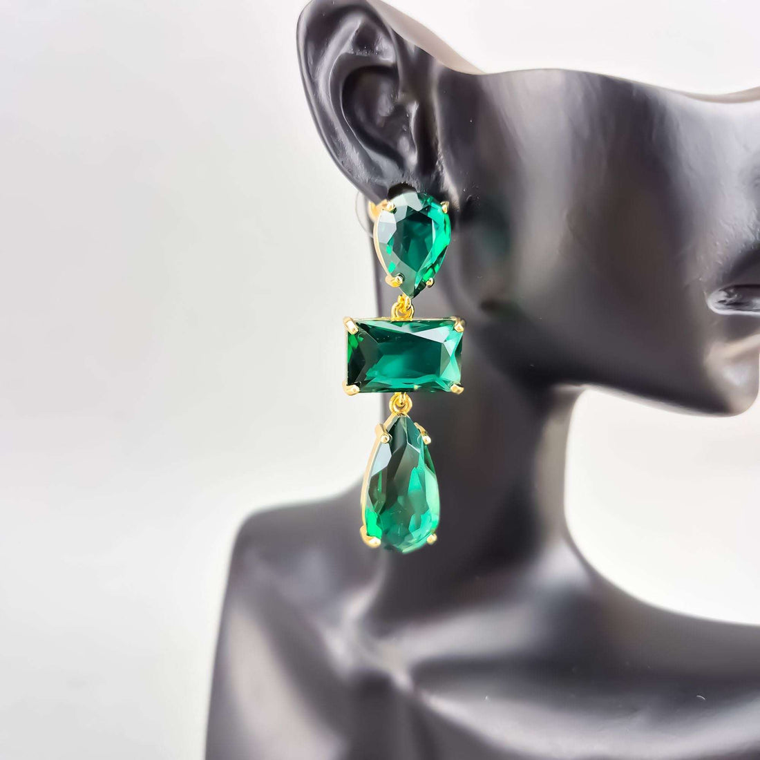 Длинные серьги с тремя изумрудно-зелёными кристаллами в позолоченной оправе, надетые на ухо манекена