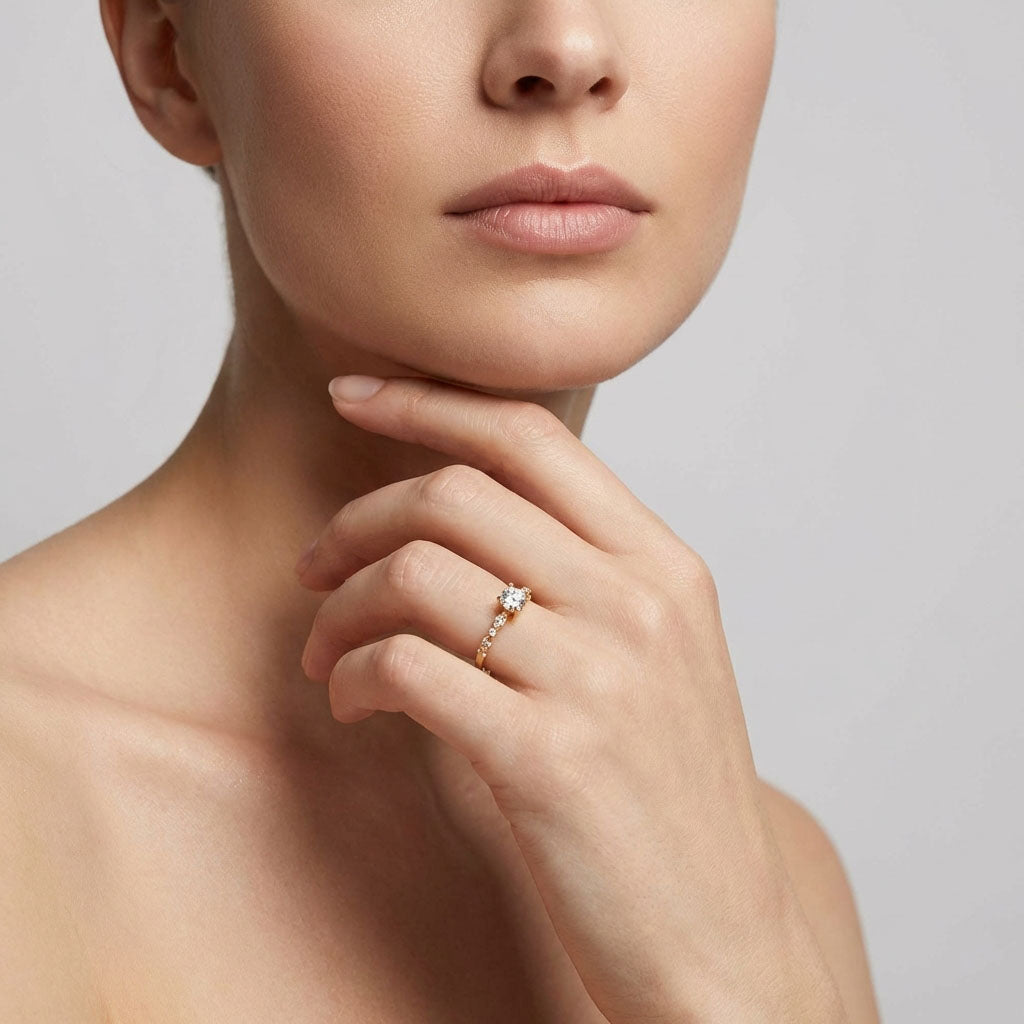 Modelė mūvi paauksuotą žiedą su baltu cirkoniu, ranką pakėlusi prie smakro