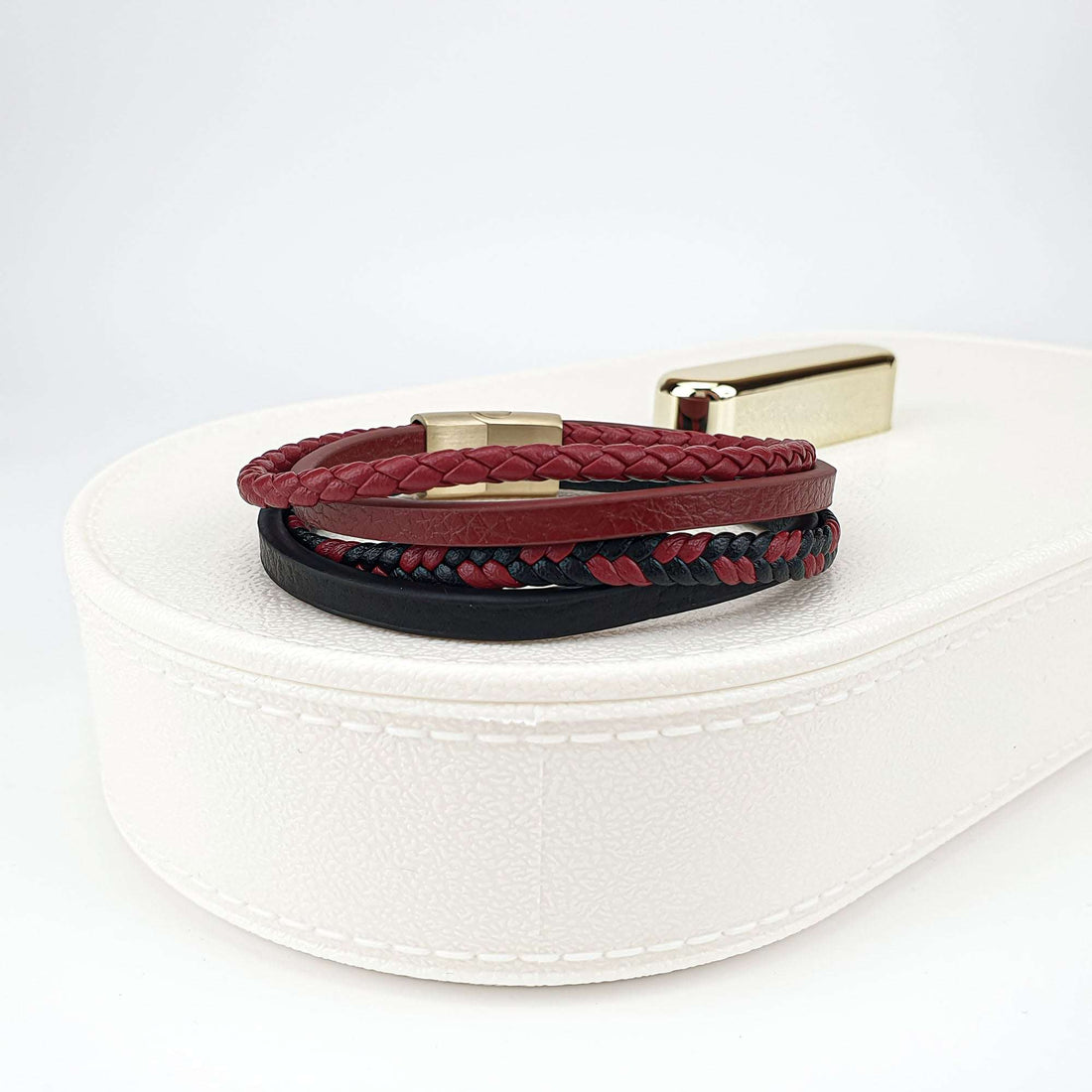 Красно-чёрный кожаный браслет с плетёными и гладкими ремешками на белой шкатулке для украшений