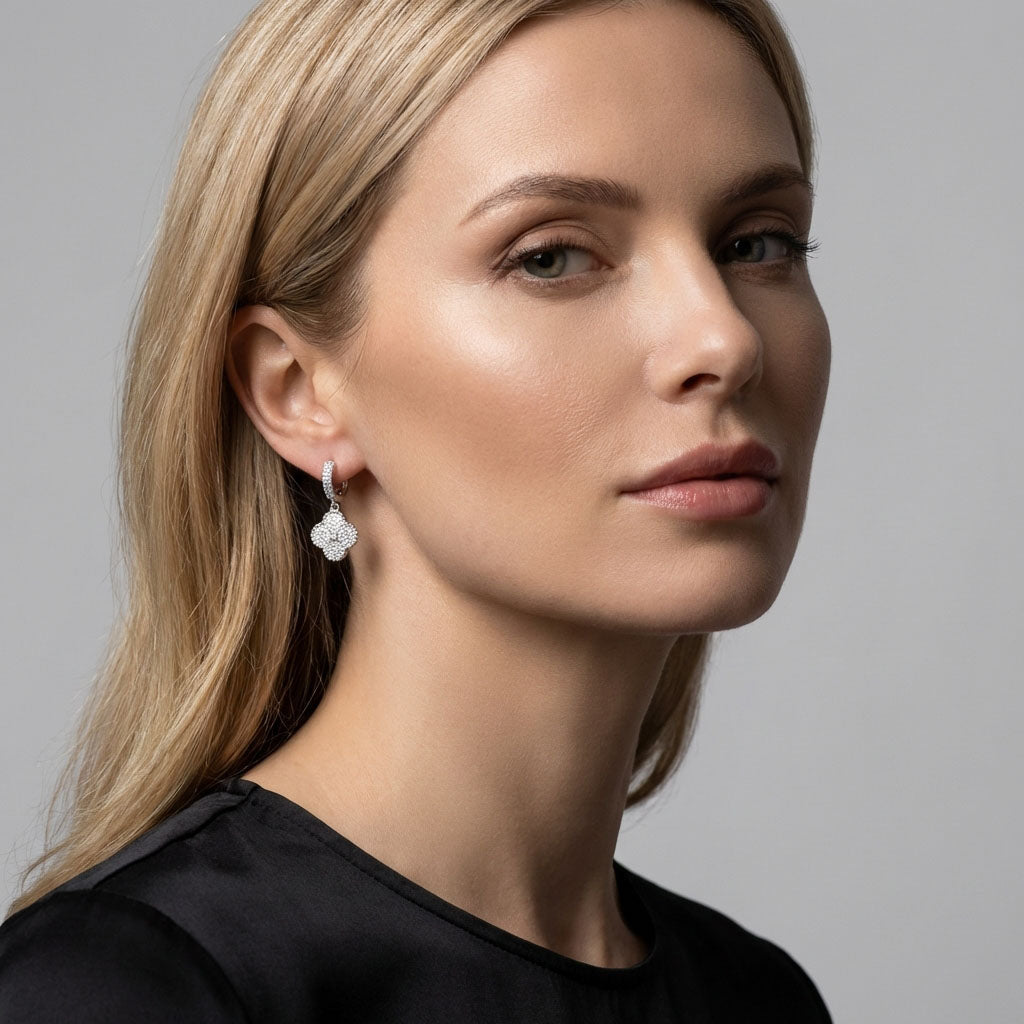 Modelė juodu topu su kabančiu dobilo auskaru sidabro atspalvio šviesiame fone