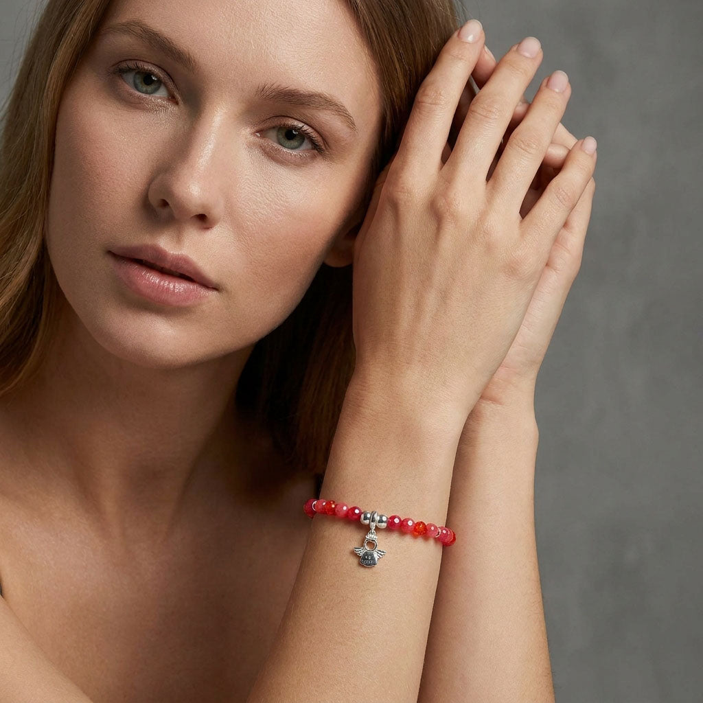 Modelė ant riešo dėvi raudonų akmenukų apyrankę su angelo pakabučiu