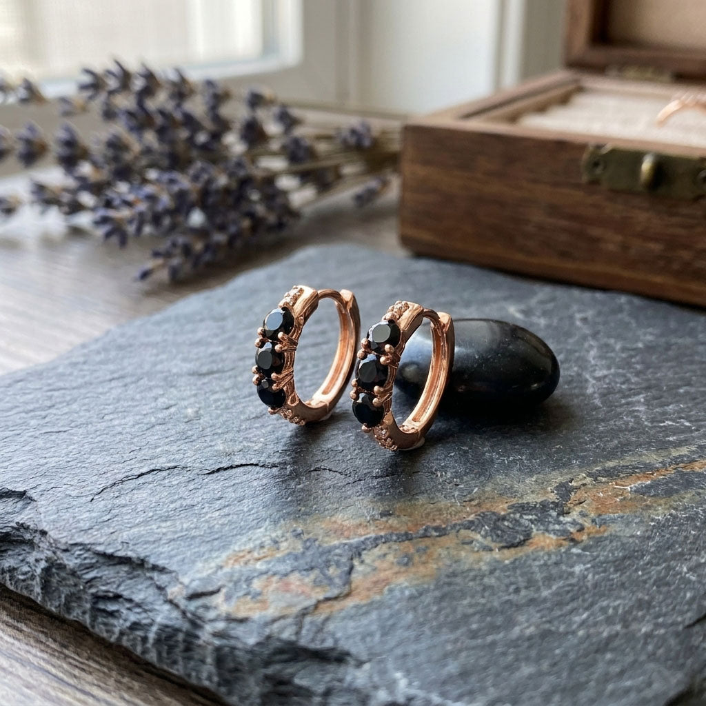 Nelieli apzeltīti sieviešu auskari ar tumšiem akmeņiem rindā