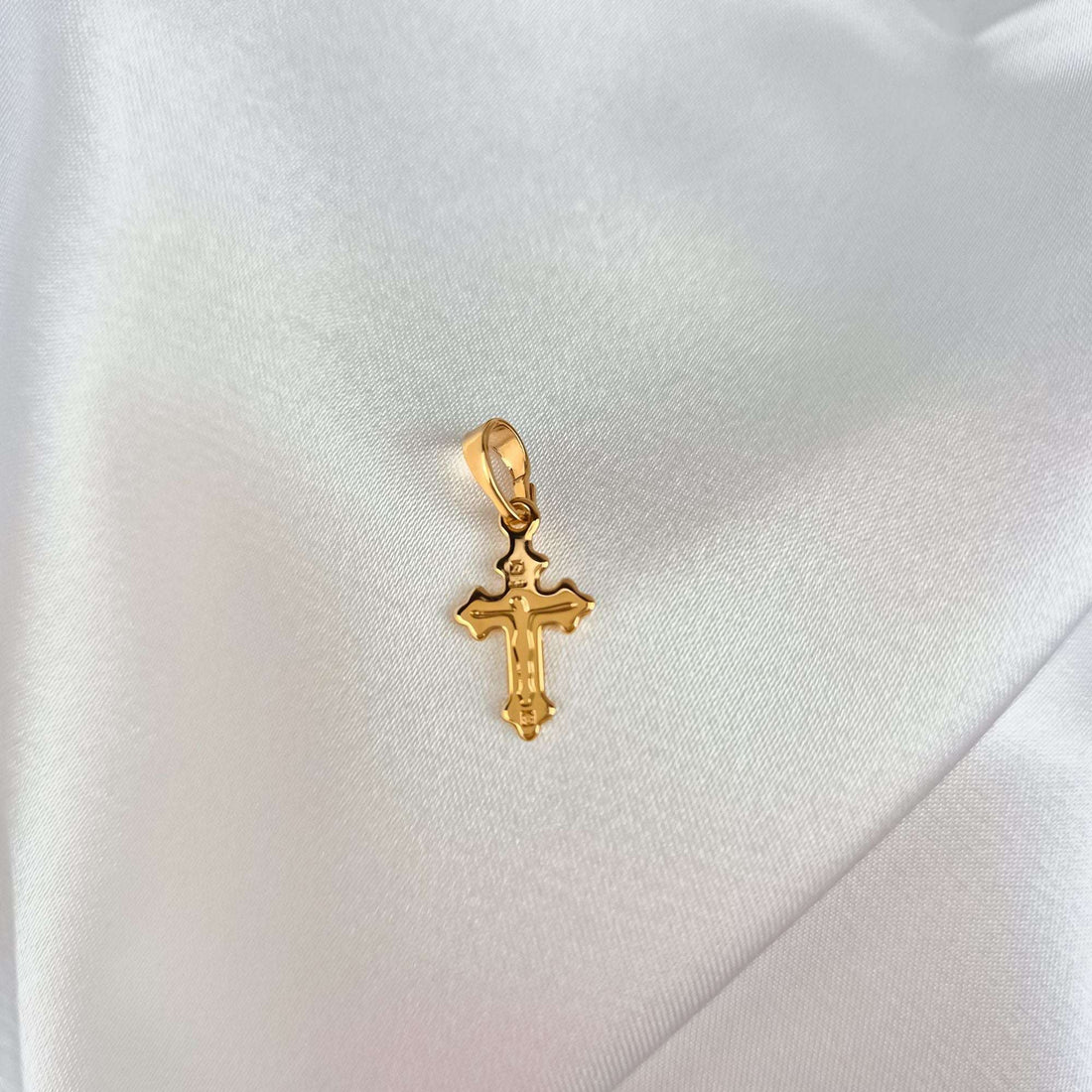 Grakštus paauksuotas 21 mm kryželis su nukryžiuotojo reljefu ant balto satino audinio