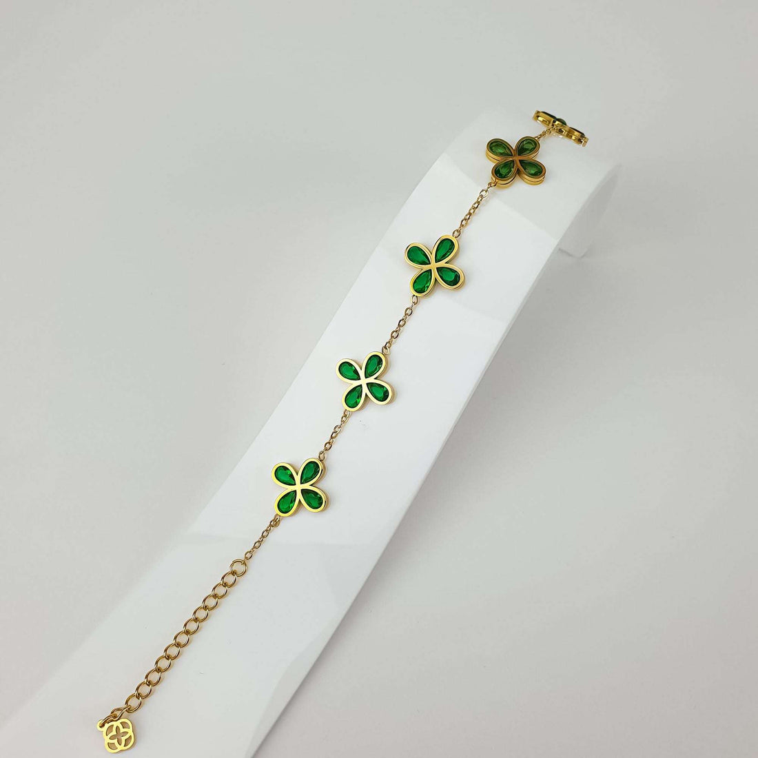 Браслет с клевером и зелёными кристаллами на подставке, видна цепочка и регулируемый удлинитель
